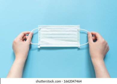 Hands Holding Protective Medical Face Mask On Light Blue Background. Devices Designed To Protect The Wearer From Inhaling Airborne Bacteria, Virus Or Dust Particles. Health Care. Top View.