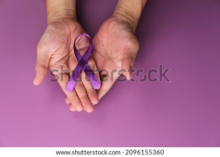Hands holding Purple ribbons on a purple background. Alzheimer's disease, pancreatic cancer, epilepsy awareness, fibromyalgia awareness. World cancer day concept. Copy space.
