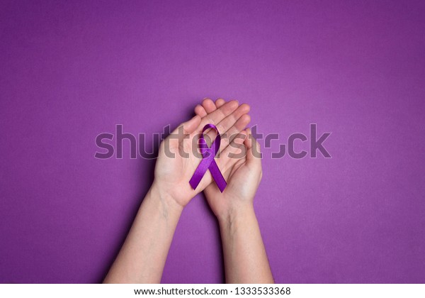 Hands holding Purple ribbons on a\
purple background. World epilepsy day. Alzheimer\'s disease,\
Pancreatic cancer, Epilepsy awareness, fibromyalgia\
awareness.