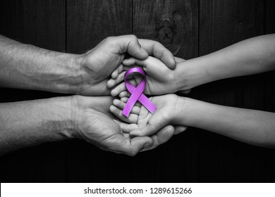 Hands holding purple ribbons top view on black wooden background. Alzheimer's disease, epilepsy, fibromyalgia awareness, world cancer day. black and white. symbol of fighting child abuse.