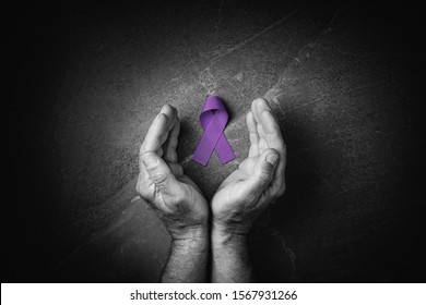 Hands Holding Purple Ribbons Top View On Dark Gray Background. Alzheimers Disease, Epilepsy, Fibromyalgia Awareness, World Cancer Day. Black And White. Symbol Of Fighting Child Abuse.