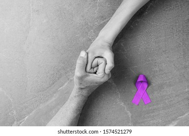 Hands Holding Purple Ribbons Top View On Gray Wooden Background. Alzheimers Disease, Epilepsy, Fibromyalgia Awareness, World Cancer Day. Black And White. Symbol Of Fighting Child Abuse.