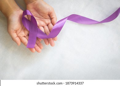 Hands holding purple or violet ribbon on white fabric with copy space. Pancreatic Cancer ,Testicular Cancer Awareness, Cancer Survivor, Leiomyosarcoma, World Cancer Day. Healthcare, insurance concept.