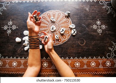 hands holding runes stones on an ornate table