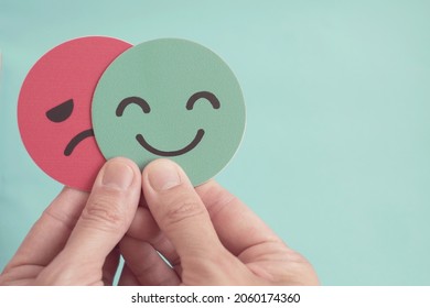 Hands holding sad face hiding behind happy face, bipolar and depression, mental health, split personality,  mood change,  - Shutterstock ID 2060174360