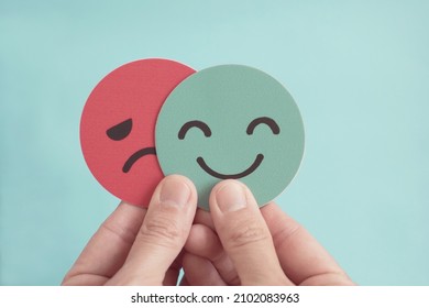 Hands holding sad face hiding behind happy face, bipolar and depression, mental health, split personality,  mood change concept