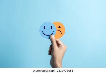 Hands holding sad face hiding or behind happy smiley face, bipolar and depression, mental health concept, personality, mood change, therapy healing split concept.