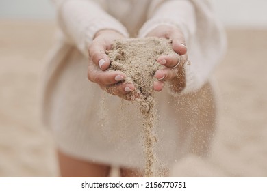 Hands holding sand on background of beach, carefree moment. Stylish young woman in sweater releasing sand on coast. Sand running through hands. Time concept. Summer beach and vacation - Powered by Shutterstock