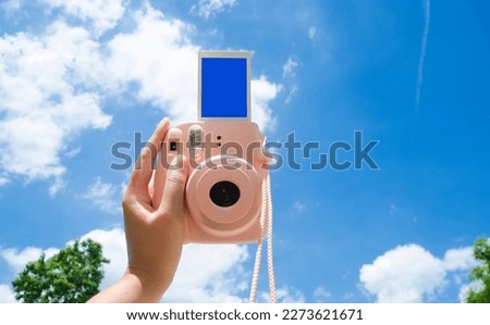 Hands Holding and shooting an empty screen photo frame Instant Camera with blue sky view on background.