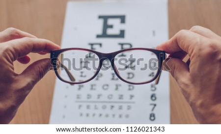 Hands holding sight glasses in front of optician sight chart. 