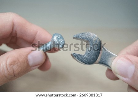 hands holding a silver bolt with a hexagonal head in one hand and a small open-end wrench in the other, seemingly preparing to tighten or loosen the bolt.