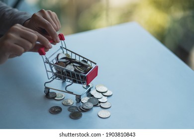 Hands holding a small shopping cart full of coins for saving money and financial concept