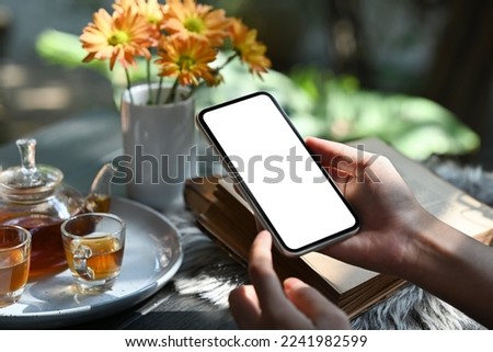 Hands holding smart phone against traditional tea set with cups and teapot on rustic wooden table. Close up view