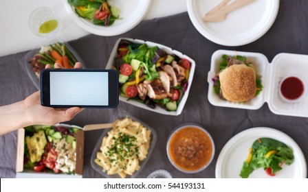 Hands Holding Smartphone Mobile Cellphone Over Different Types Of Gourmet Takeout, Food Delivery Order App Application Concept