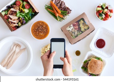 Hands Holding Smartphone Mobile Cellphone Over Different Types Of Gourmet Takeout, Food Delivery Order App Application Concept