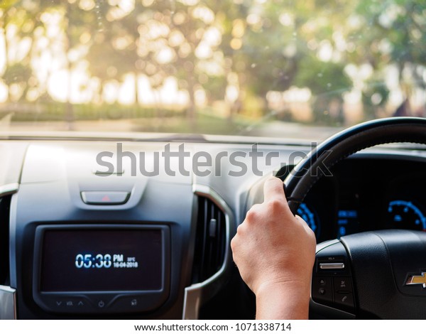 Manâ??s hands holding steering wheel and blur\
trees background. Driving\
concept