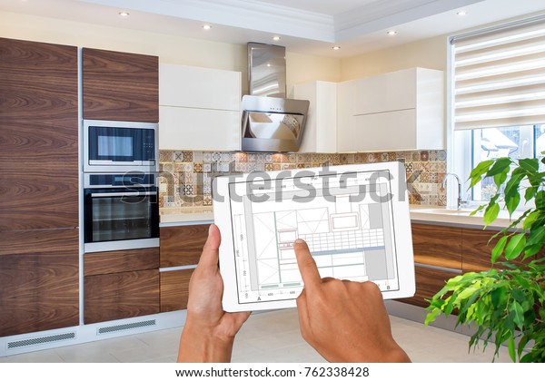 Hands holding tablet showing kitchen plans in finished room. Modern