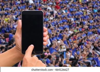 Hands Holding And Touch Screen Smart Phone On Soccer Fans In A Match And Spectators At Football Stadium