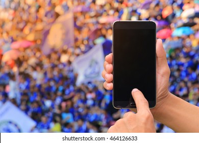 Hands Holding And Touch Screen Smart Phone On Soccer Fans In A Match And Spectators At Football Stadium