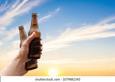 Hands holding two beer bottles and happy enjoying harvest time together to clinking glasses at outdoor party on beautiful sunset background.Celebration drinking beer.        - Powered by Shutterstock