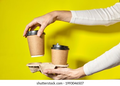 Hands Holding Two Cups Brown Paper With Black Lid. Two Coffee Special Offer Or Promo. Hands Holding Two Cups On Yellow Screen Background. Tea Or Coffee To Go. Brown Paper Cup With Black Lid.