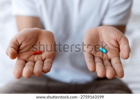 Hands holding two different colored capsules, symbolizing decision, options, and paths