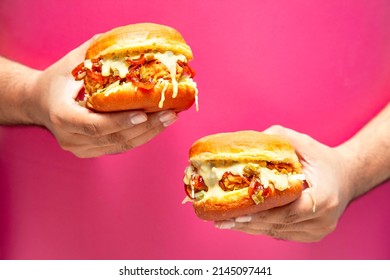 Hands holding two fried chicken on a pink coloured background. 