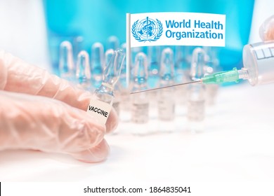 Hands Holding A Vaccine Vial And A Syringe, Rows Of Capsules And A Flag Of WHO (World Health Organization), Illustrating COVAX Facilities' Plans For Global Vaccination Against Covid-19 (SARS-CoV-2).