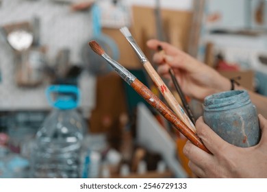 Hands holding well used paintbrushes and a colorful palette in a vibrant art studio - Powered by Shutterstock