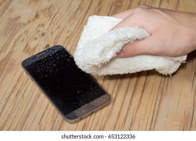 Hands holding White cloth with wet smartphone drops on wooden floor