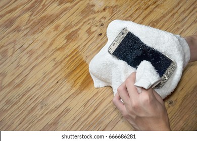 Hands holding White cloth with wet smart phone drops on wooden floor