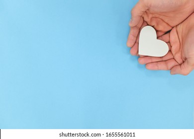 Hands holding a white heart in blue background with copy space. Kindness, charity, pure love and compassion concept.