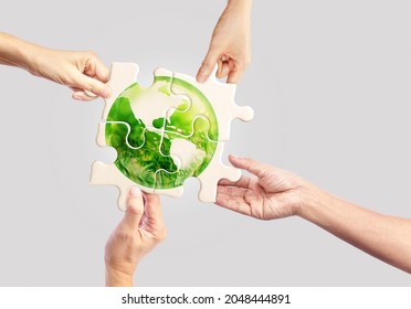 Hands holding white jigsaw with globe glass earth with green grass field in side on light pastel background, Friendly World Sustainable Environment Natural Day and Save our Earth Concept
