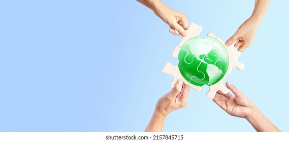 Hands holding white jigsaw with green globe glass earth on light pastel background - Shutterstock ID 2157845715