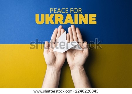 hands holding white paper dove with words peace for Ukraine on background of yellow and blue flag of ukraine. truth will win