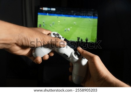 Hands holding a wireless game controller playing a soccer video game on a television screen