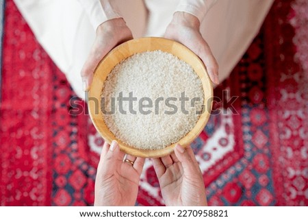 Hands holding a wooden bowl of rice grains for zakat, Islamic zakat concept. Muslims to help the poor and needy. Conceptual shoot for property, income, and fitrah zakat.