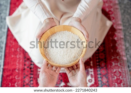 Hands holding a wooden bowl of rice grains for zakat, Islamic zakat concept. Muslims to help the poor and needy. Conceptual shoot for property, income, and fitrah zakat.