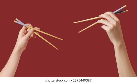 Hands holding wooden chopsticks on red background