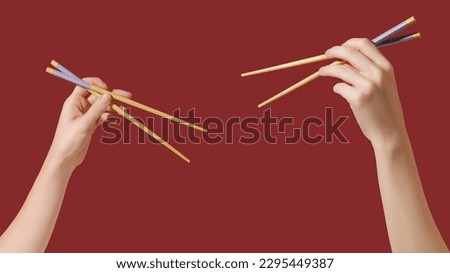 Hands holding wooden chopsticks on red background