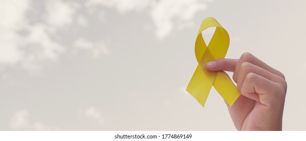 Hands holding yellow gold ribbon over grey sky, Sarcoma Awareness, Bone cancer, childhood cancer awareness, September yellow, World Suicide Prevention Day concept