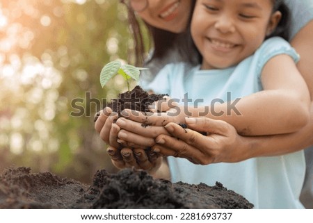 hands holding young plant with soil.World environment day and sustainable environment concept. Mom and her child girl plant sapling tree. Teamwork protecting and reduce global warming earth.