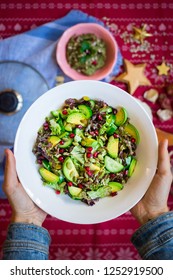 Hands Holds Big Bowl Fresh Green Salad With Avocado, Spinach, Cucumbers, Pomegranate Grains. Vegan Vegetarian Christmas Lunch, Dinner Food On Red Tablecloth