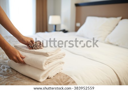 Hands of hotel maid putting flowers on the stack of towels