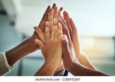 Hands, huddle and high five while a group of diverse businesspeople celebrate and motivate each other at the workplace. Colleagues winning and achieving success through teamwork and collaboration