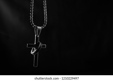 Hands of human praying on black background. A silver cross with a silver ring attached and a light shining down in the dark. Religion concept. - Shutterstock ID 1210229497