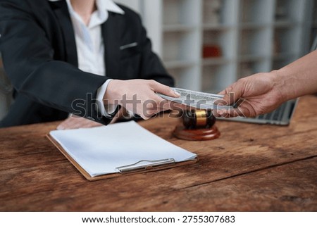 Hands of individuals exchanging a stack of paper currency at a wooden desk, symbolizing bribery, illegal payments, and financial crime in a legal or business context with a gavel nearby