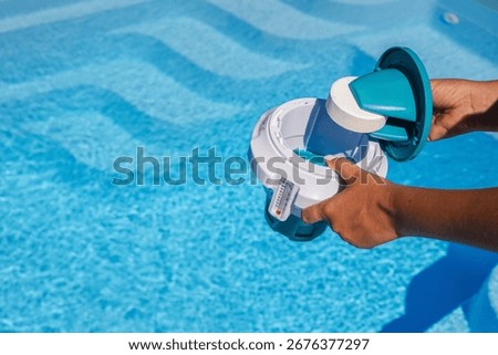 Hands inserting chlorine tablet into floating pool dispenser for clean and safe swimming water. High quality photo