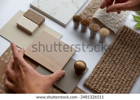 Hands of Interior Designer and Architect with Material Sample Board with Fabrics, Carrara Marble, Wood, and Wallpaper for Home Decoration Mood Board Concept