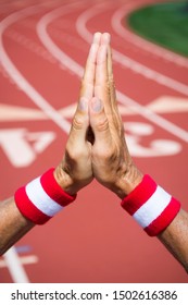 Hands Of Japanese Athlete Wearing Red And White Colored Wristbands Making Hopeful Prayer Gesture Of Gratitude Against A Red Athletic Track Background